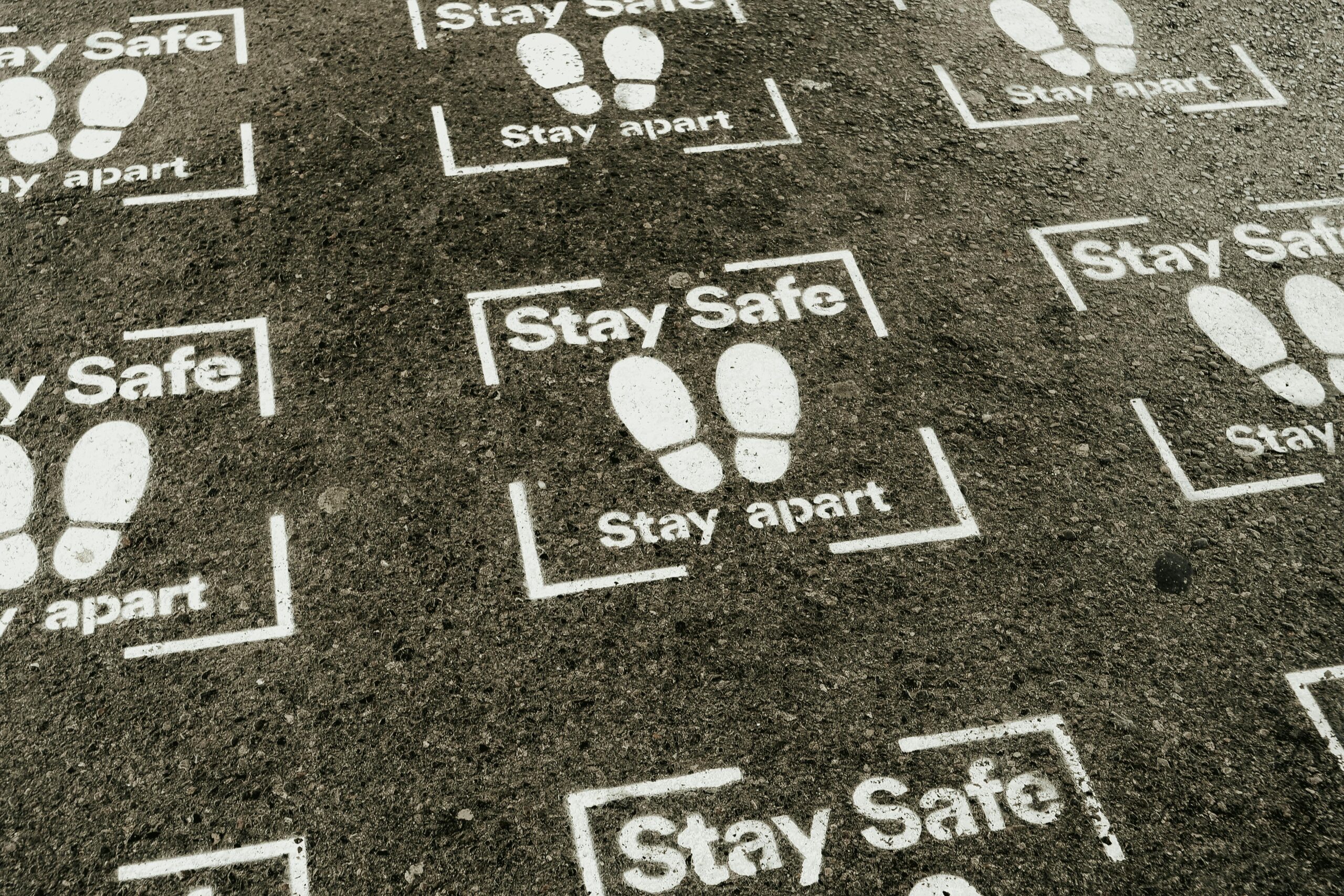 From above white sign of feet and inscription Stay Safe Stay Apart painted on asphalt road during coronavirus outbreak