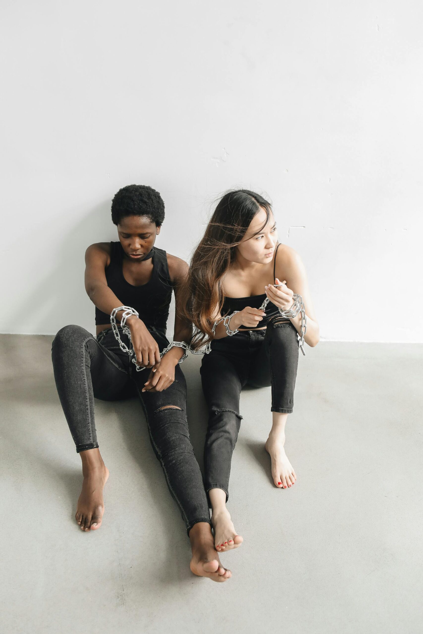Two women sitting in chains symbolizing struggle and resilience, shot indoors with natural light.